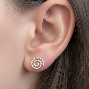 Peut inclure: Gros plan sur une oreille ornée d'une boucle d'oreille en forme de spirale argentée. Le bijou présente un design minimaliste et la forme en spirale est clairement visible. Un petit bijou délicat.