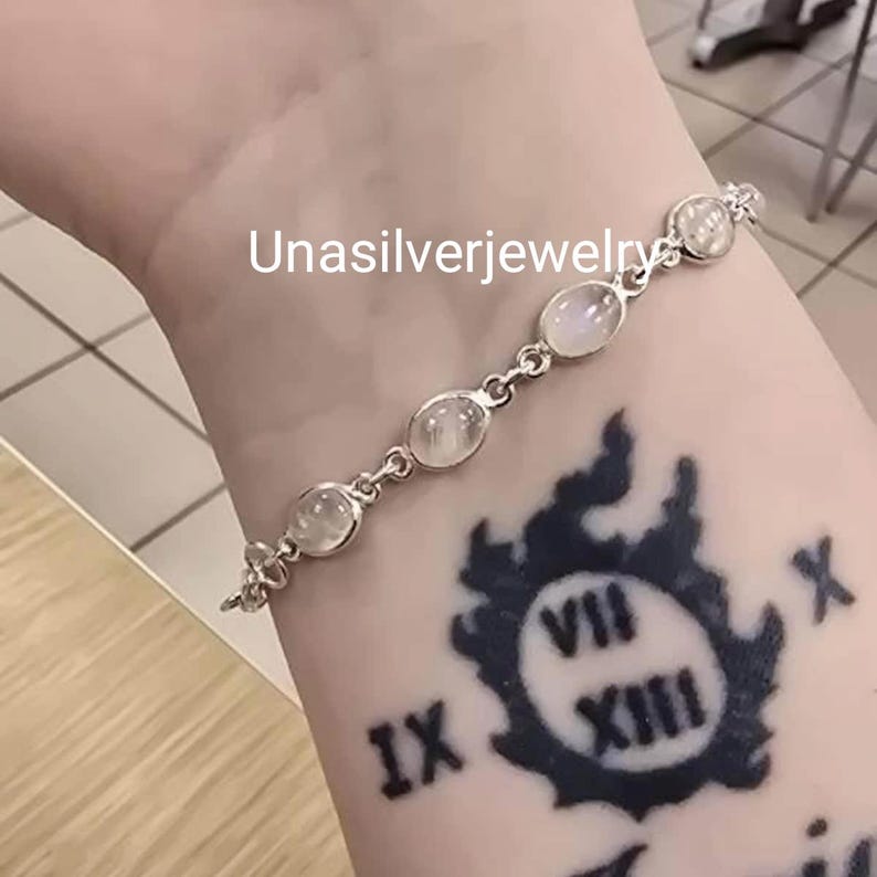 May include: A silver bracelet featuring oval-shaped, translucent gemstones. The bracelet is connected by small, decorative links. The text "Unasilverjewelry" is visible. The bracelet is worn on an arm with a tattoo.