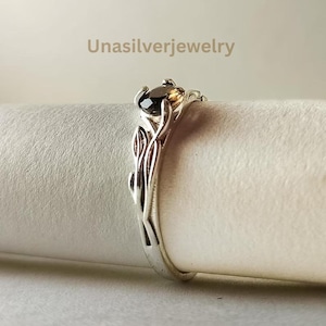 Op de afbeelding: Een zilveren ring met een donkerbruine, ovale edelsteen in een klauwzetting. De ringband is ontworpen met een sculpturaal blad- of rankmotief. De tekst Unasilverjewelry is zichtbaar in het bovenste gedeelte van de afbeelding boven de ring.