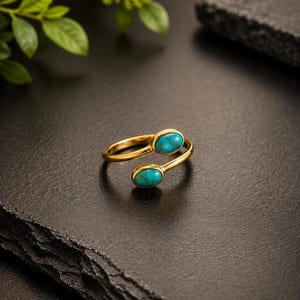 May include: An open-style gold ring featuring two oval-shaped turquoise stones. The band is polished gold, and the two stones are set at each end of the open gap, creating a bypass design with vibrant blue-green cabochons.