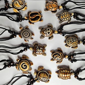 May include: A collection of turtle pendant necklaces. Each pendant is a different design in shades of brown and cream, strung on a black cord with wooden beads. The turtle designs include spirals, geometric patterns, and a yin-yang symbol.