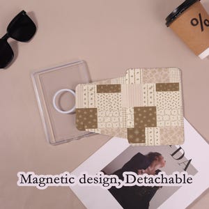 May include: A clear phone case with a white ring grip and a patterned phone cover. The cover features a patchwork design in shades of brown and beige. Sunglasses and a coffee cup are also visible.