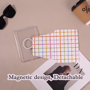 Może przedstawiać: Przezroczyste etui na telefon z białym uchwytem w kształcie pierścienia i odpinanym uchwytem na karty. Uchwyt na karty ma białe tło z kolorowym wzorem w kratę. Widoczny jest tekst "Magnetic design, Detachable".