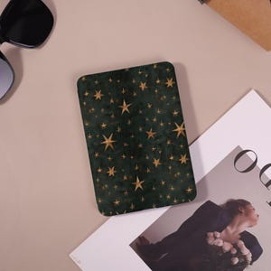 May include: A rectangular, dark green coaster with a pattern of gold stars of varying sizes. The coaster has rounded corners and a slightly textured appearance. The stars are scattered across the surface, creating a celestial design.