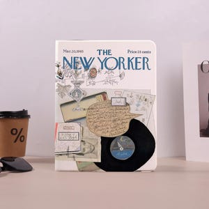 May include: A white notebook with a vintage "New Yorker" cover, featuring the magazine's logo and the date "Mar.20,1965". The cover is adorned with illustrations, a vinyl record, and handwritten notes. A coffee cup with a percentage symbol is visible.
