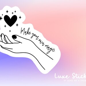May include: Black and white illustration of a hand holding a heart with stars around it. The text "Make your own magic." is written in cursive below the hand. The background is a gradient of pink and purple.