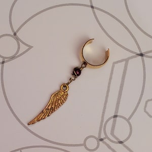 May include: Gold ear cuff with a dangling gold wing charm and a dark purple bead.