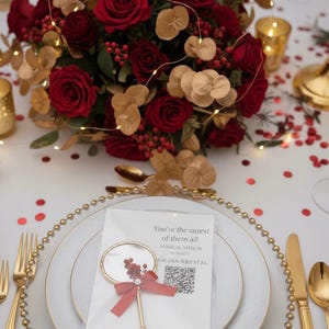 Pu&ograve; includere: Elegante mise en place con un centrotavola di rose rosse e dettagli dorati. Ogni posto a tavola comprende un piatto bianco con bordi dorati, posate dorate e un segnaposto a specchio decorativo con un fiocco rosso. Il testo sul segnaposto recita "You're the rarest of them all".