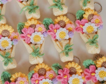 Può includere: Una collezione di bouquet di fiori all'uncinetto fatti a mano, con girasoli gialli, margherite rosa e bianche e accenti viola. Ogni bouquet è avvolto in un cono giallo chiaro e ha foglie verdi.