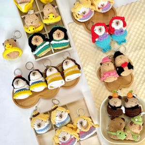 May include: A collection of handmade crochet keychains featuring various character designs. The keychains showcase a variety of colors, including yellow, blue, red, and brown. Each keychain has a metal ring for easy attachment to keys or bags.