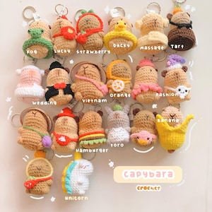 May include: A collection of 15 crocheted capybara keychains in various costumes, including a wedding dress, a banana, a hamburger, a unicorn, and a duck. The keychains are displayed on a white background with the text "capybara crochet" below them.