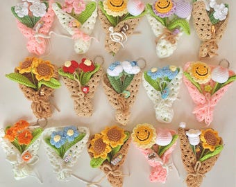 Può includere: Una collezione di 18 bouquet di fiori all'uncinetto, ognuno con un colore e un design diverso. I bouquet sono realizzati con filato di vari colori, tra cui rosa, blu, giallo, verde e bianco. Ogni bouquet è legato con un nastro e ha un piccolo anello di metallo attaccato alla parte superiore.