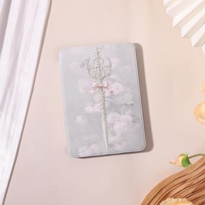 Pode incluir: Bandeja decorativa retangular azul claro com um design floral com uma espada decorativa e um laço rosa. O fundo tem um padrão floral suave e desfocado em tons de rosa e branco.