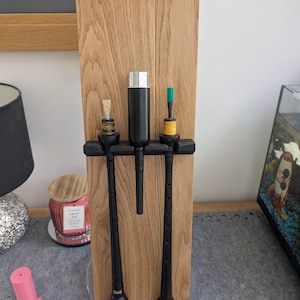 May include: Three black bagpipes with a black and silver cleaning kit on a wooden stand. The stand has a clear base.