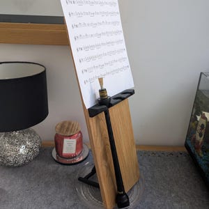 May include: A black wooden stand with a sheet of music titled "Paddy's Leather Breeches" on top. A black wooden pipe is leaning against the stand. A black wooden pipe is lying on a gray surface.