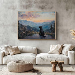 Pode incluir: Pintura emoldurada de um c&atilde;o preto contemplando uma paisagem montanhosa ao p&ocirc;r do sol. A obra de arte est&aacute; pendurada acima de um sof&aacute; branco com almofadas bege. Um pufe tecido e uma mesa lateral de madeira completam a cena.
