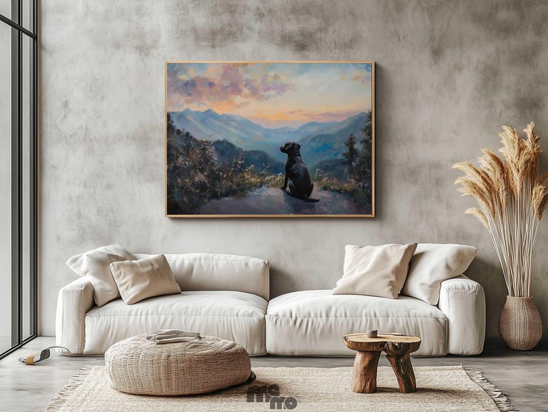Pode incluir: Pintura emoldurada de um c&atilde;o preto contemplando uma paisagem montanhosa ao p&ocirc;r do sol. A obra de arte est&aacute; pendurada acima de um sof&aacute; branco com almofadas bege. Um pufe tecido e uma mesa lateral de madeira completam a cena.