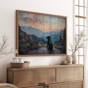 Pode incluir: Pintura de paisagem emoldurada que retrata um c&atilde;o preto olhando para uma cordilheira ao p&ocirc;r do sol. A obra de arte &eacute; exibida acima de um arm&aacute;rio de madeira com itens decorativos.