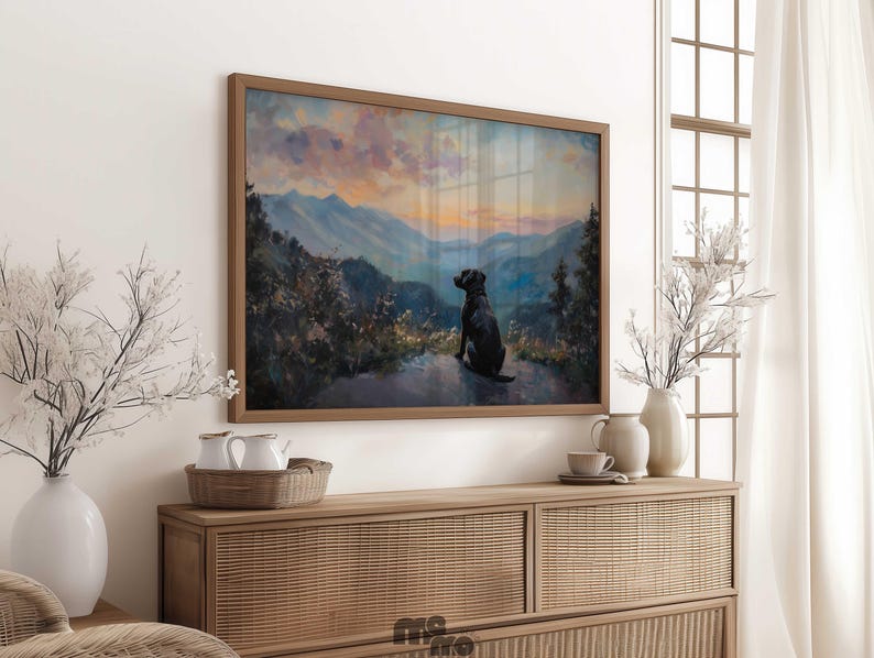 Pode incluir: Pintura de paisagem emoldurada que retrata um c&atilde;o preto olhando para uma cordilheira ao p&ocirc;r do sol. A obra de arte &eacute; exibida acima de um arm&aacute;rio de madeira com itens decorativos.