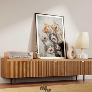 May include: A framed art print featuring a group of laughing cats in various colors, displayed on a wooden cabinet. The cabinet has a ribbed design and is accompanied by a lamp, a vase, and a vintage stereo. The scene is set against a neutral wall.