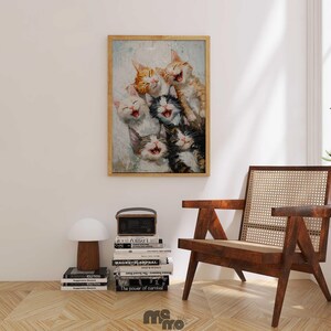 May include: A framed print featuring a group of laughing kittens in various colors, including orange, white, and black. The artwork is displayed on a white wall above a wooden chair and a stack of books.