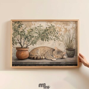 May include: A framed print featuring a sleeping tabby cat. The cat rests on a ledge, with potted plants on either side. The artwork has a neutral color palette with a vintage aesthetic, and is set against a textured background.