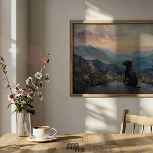 Pode incluir: Uma pintura de paisagem emoldurada retrata um c&atilde;o preto olhando para uma cordilheira ao p&ocirc;r do sol. A obra de arte est&aacute; em uma moldura de madeira e pendurada em uma parede branca. Uma mesa de madeira em primeiro plano cont&eacute;m um vaso de flores e uma x&iacute;cara de caf&eacute;.
