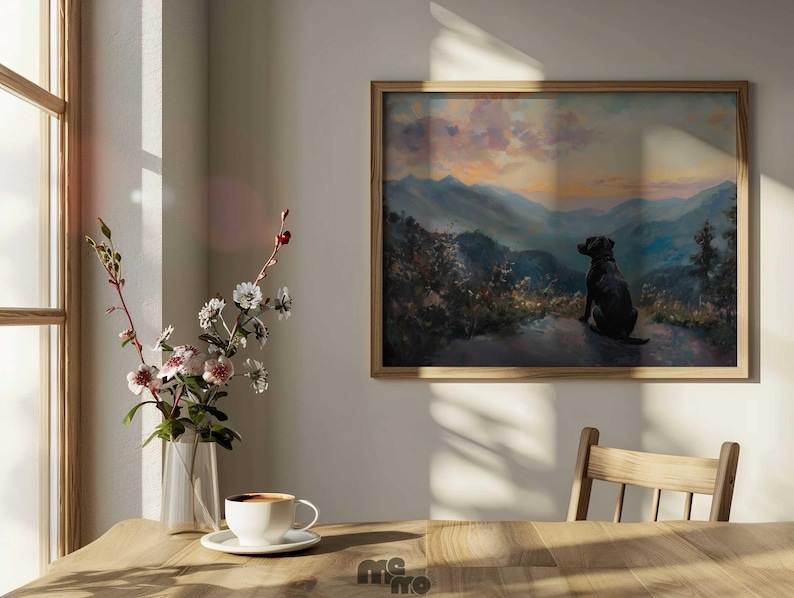 Pode incluir: Uma pintura de paisagem emoldurada retrata um c&atilde;o preto olhando para uma cordilheira ao p&ocirc;r do sol. A obra de arte est&aacute; em uma moldura de madeira e pendurada em uma parede branca. Uma mesa de madeira em primeiro plano cont&eacute;m um vaso de flores e uma x&iacute;cara de caf&eacute;.