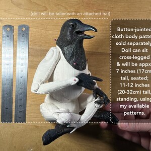 May include: A black and white articulated doll with a raven head, sitting cross-legged. The doll is 7 inches (17 cm) tall when seated and 11-12 inches (20-32 cm) tall when standing. The doll's body pattern is sold separately.  (doll will be taller with an attached hat)