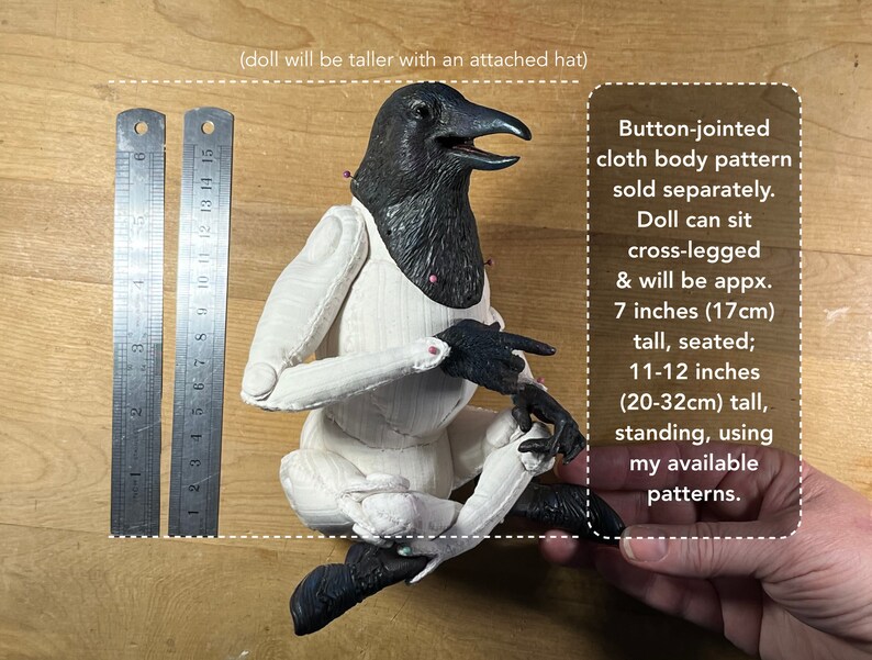 May include: A black and white articulated doll with a raven head, sitting cross-legged. The doll is 7 inches (17 cm) tall when seated and 11-12 inches (20-32 cm) tall when standing. The doll's body pattern is sold separately.  (doll will be taller with an attached hat)