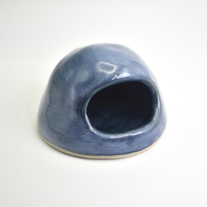 May include: A dome-shaped ceramic salt cellar with a smooth, glossy finish in shades of blue and grey. The object features a wide, rounded opening on the front side, revealing a dark interior, and sits on a flat, circular base with a light-coloured rim.
