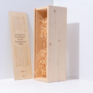 Può includere: Una scatola di vino in legno chiaro con coperchio, riempita di paglia. Il coperchio presenta il testo "Fantastische Feestdagen en een Sprankelend 2024". La scatola è aperta, rivelando la paglia all'interno. La scatola è in legno chiaro.