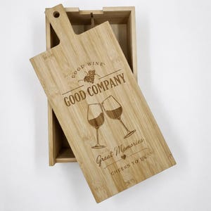 Könnte beinhalten: Eine Weinkiste aus Bambus mit einem Deckel aus Holz in Form eines Schneidebretts. Der Deckel ist mit den Worten "Good Wine Good Company Great Memories Cheers to Us" graviert und zeigt zwei Weingläser. Die Kiste ist geöffnet.