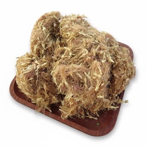 May include: A pile of dried, fibrous material with a light brown color and a tangled texture, resting on a small, dark wooden tray. The material appears to be plant-based, possibly for crafting or decorative purposes.