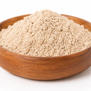 May include: A round, medium-brown wooden bowl filled with a mound of fine, light beige powder. The bowl features a visible wood grain texture and a smooth, curved rim. The powder is piled high in the centre, creating a conical shape with a textured surface.