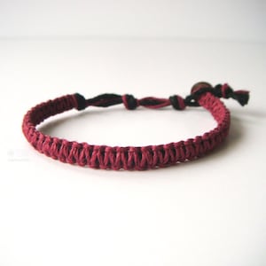 May include: A burgundy braided bracelet with a black cord and a small wooden bead.