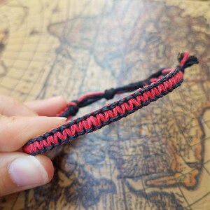 Puede incluir: Un brazalete de amistad rojo y negro hecho con cordón trenzado.