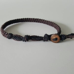 Pode incluir: Um bracelete trançado marrom e preto com fecho de botão de madeira.