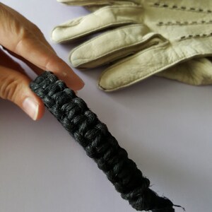 May include: A black braided rope bracelet with a thick, textured design.