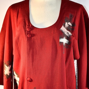 May include: A red kimono with a scoop neck and black and white abstract brushstroke designs. The kimono has three buttons down the front.