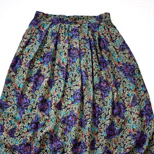 Puede incluir: Una falda midi negra con estampado floral con rosas moradas, hojas verdes y detalles azules y rojos.