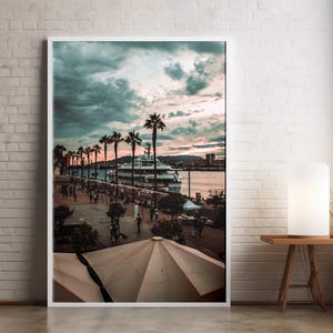 Op de afbeelding: Een wit jacht aangemeerd in een haven met palmbomen langs de waterkant. De lucht is een mix van blauw en roze met pluizige wolken. Mensen lopen langs de pier.