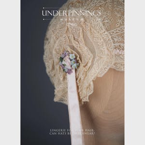 May include: A delicate, cream-colored lace hat with a pink ribbon and a floral embellishment. The hat is trimmed with lace and has a ruffled edge. The text "The Underpinnings Museum" is visible at the top of the image.