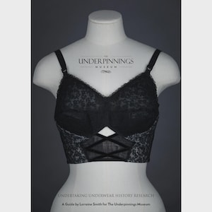 May include: Black lace bra with a criss-cross design in the center. The bra is on a white mannequin. The text "THE UNDERPINNINGS MUSEUM" is at the top of the image.