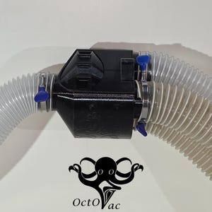 May include: A black plastic vacuum attachment with two clear, corrugated hoses connected. The hoses are secured with metal clamps and blue handles. The OctoVac logo, a black octopus, is at the bottom.