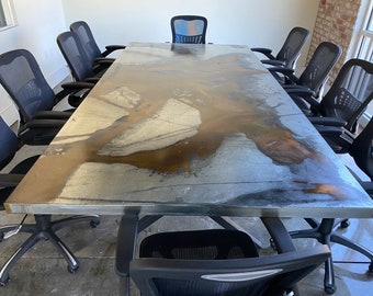 May include: A large, rectangular conference table with a silver and brown metal top. The table is surrounded by black mesh-backed office chairs.