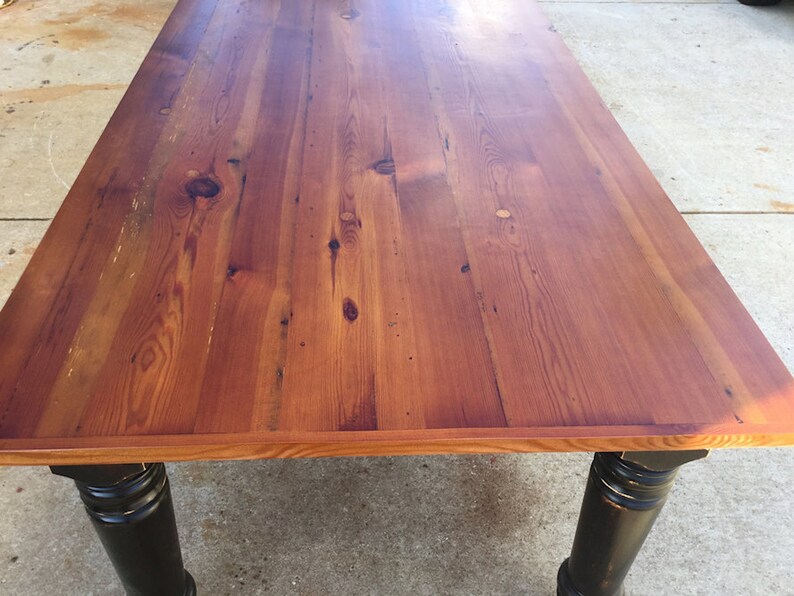 May include: A rustic wooden table with a natural wood finish and black painted legs. The table top is made of reclaimed wood planks with a smooth surface.