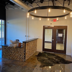 May include: A modern office lobby with a wooden reception desk, a large circular light fixture, and a cowhide rug on the floor. The sign above the double doors reads "EXIT".