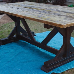 May include: A rustic wooden table with a distressed finish and a black, trestle-style base. The table is sitting on a blue moving blanket.