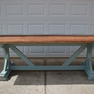 May include: A rustic wooden table with a light blue painted base. The table has a rectangular top and a trestle base with a criss-cross design.